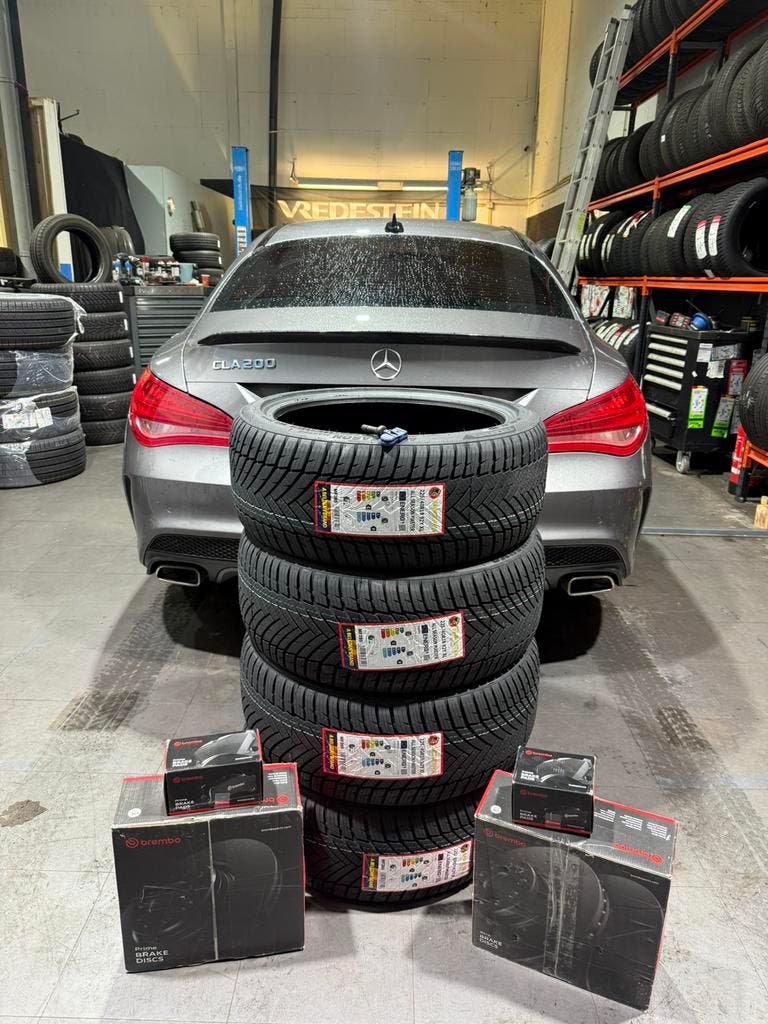Een stapel nieuwe banden en dozen met remonderdelen voor een Mercedes in de werkplaats